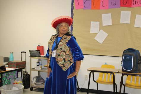Ms. Mena poses for a photo in a bright red hat and satin blue dress. She has subbed at TCHS since 1992.
